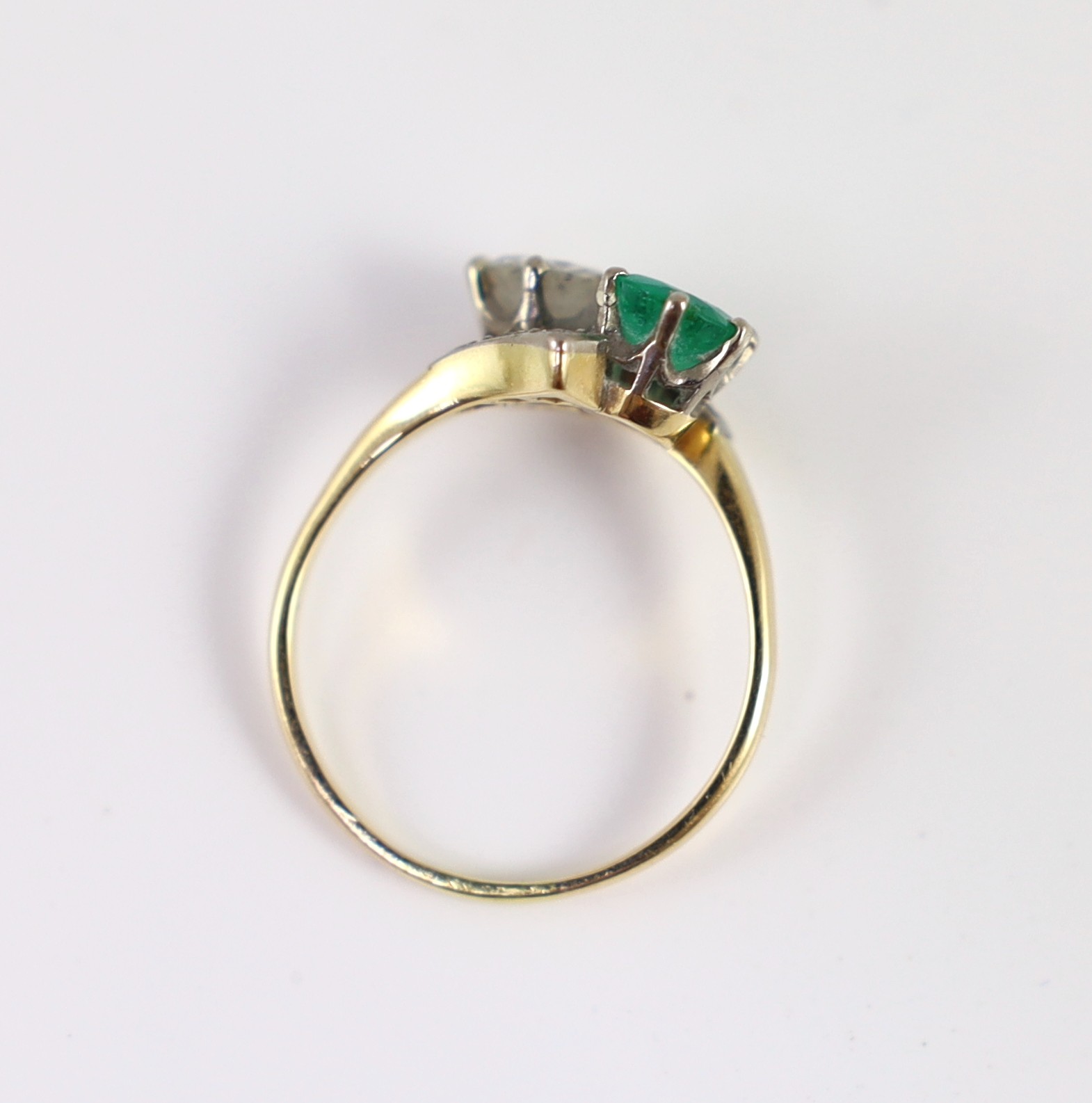 A gold, emerald and diamond set two stone cross-over ring, with diamond set shoulders